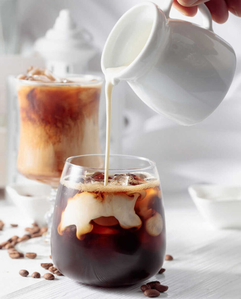 A hand is pouring the vanilla sweet cream into glass of iced and cold brew coffee